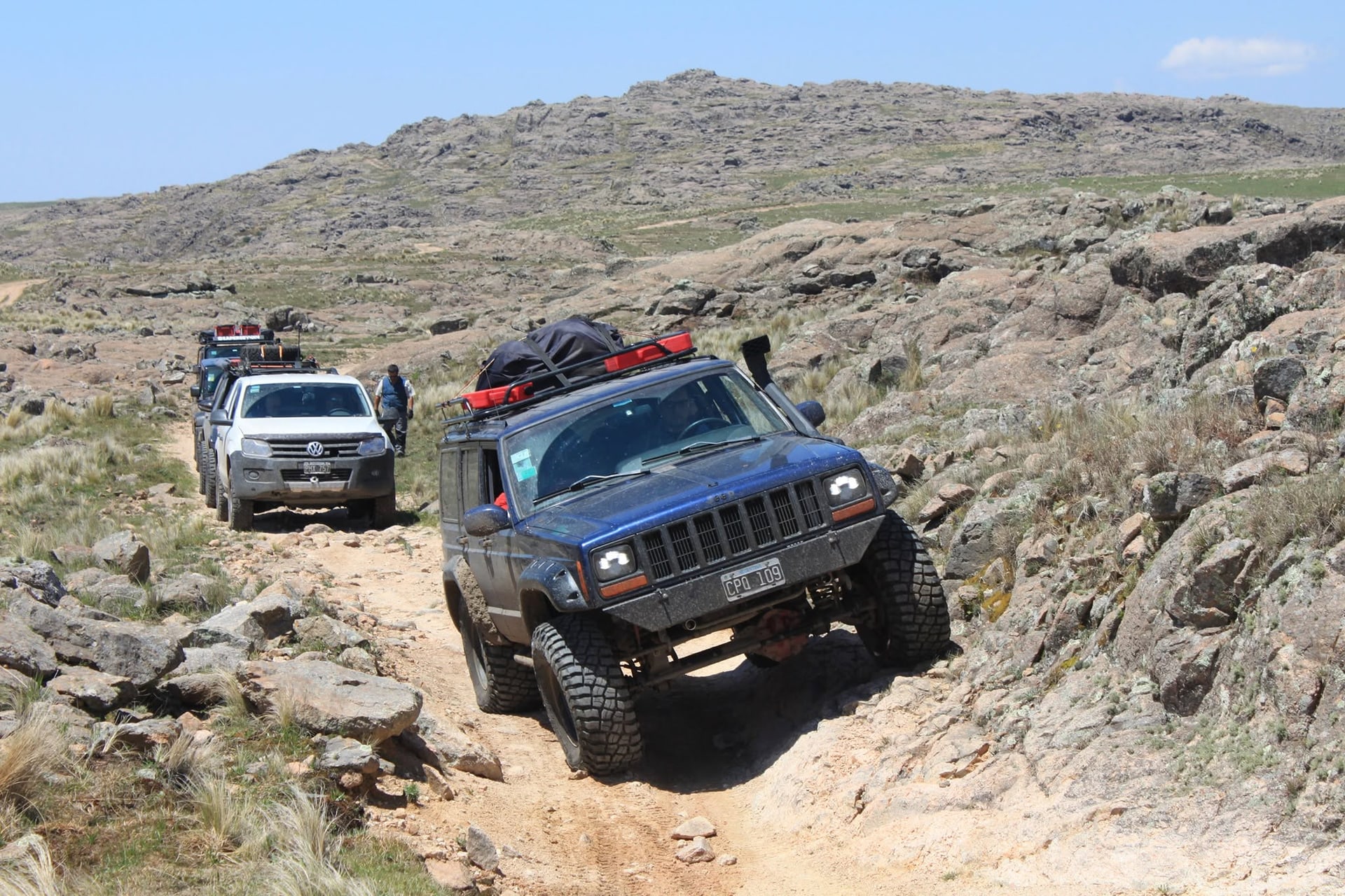 Jeep Cherokee azul encabezando una caravana en un camino de las sierras