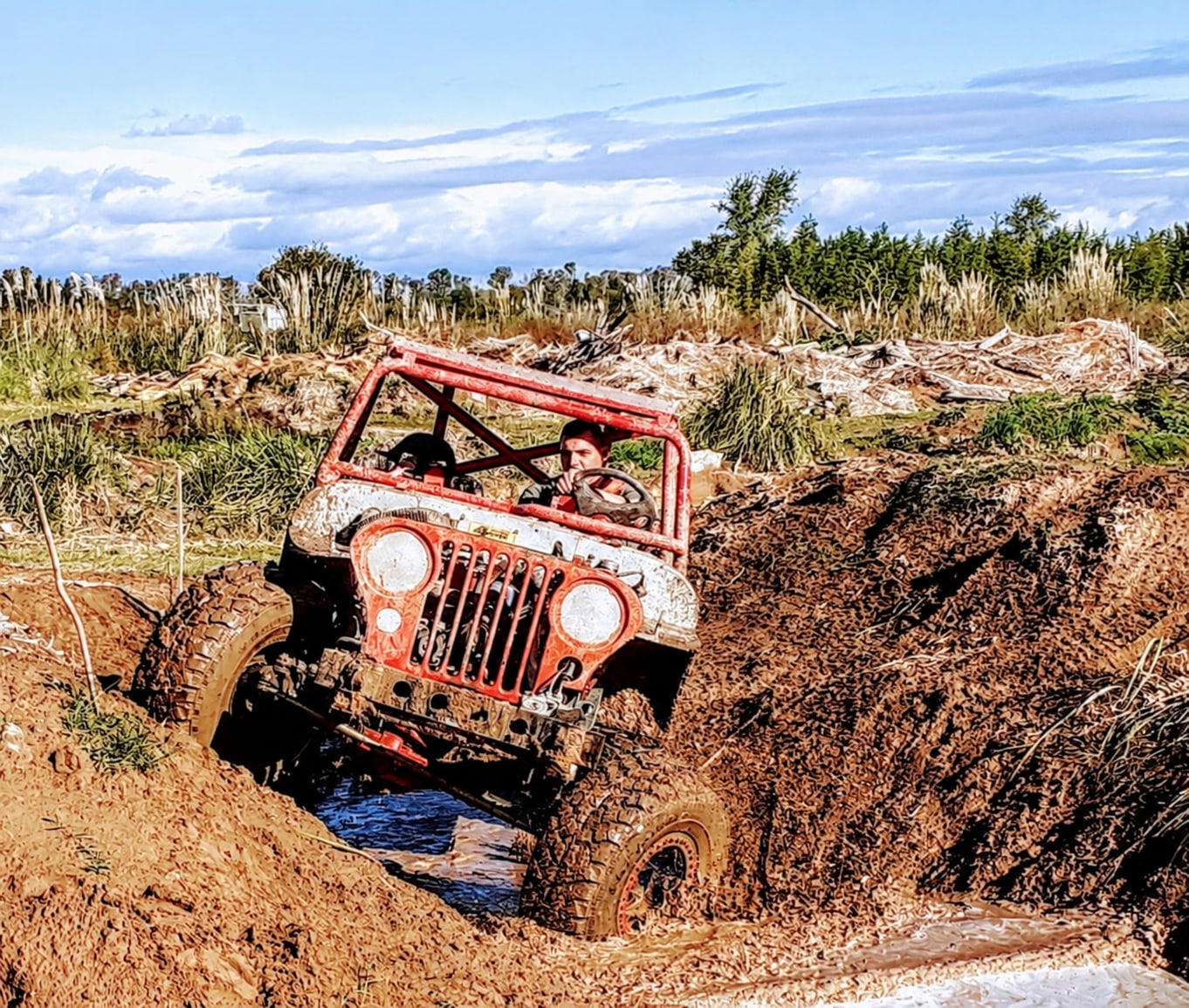Jeep rojo recorriendo un profundo surco de barro